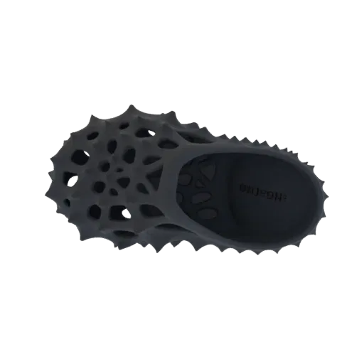 Top-down view of a dark grey, 3D model of a futuristic clog with a spiky, perforated exterior.