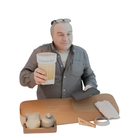 Modelo 3D de hombre con gafas, sosteniendo un vaso, de pie tras una tabla de madera con objetos.