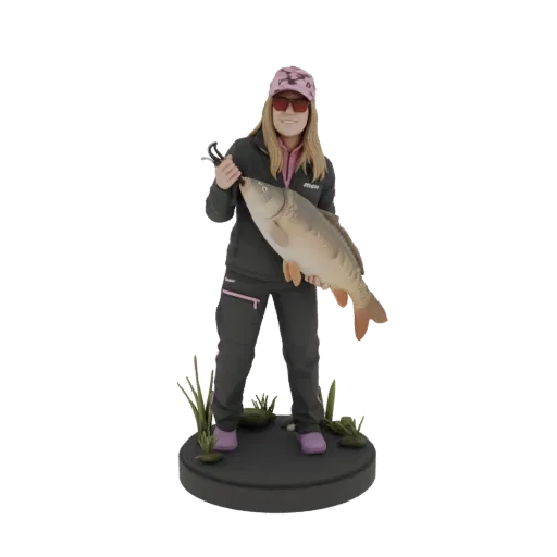 3D model of a fisherwoman in fishing gear, smiling and holding a large carp, standing on a base with grass.