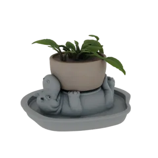Modelo 3D de un hipopótamo gris tumbado boca arriba, sosteniendo una planta en maceta encima, sobre una bandeja a juego.