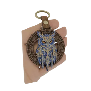 A hand holding a 3D model of a keychain featuring an ornate blue owl within a decorative medallion, with a leather strap and