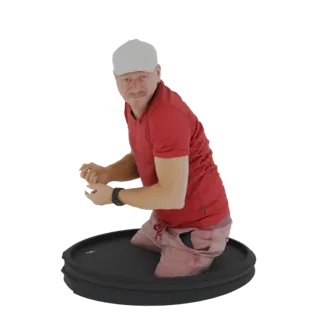 3D model of a man wearing a red polo shirt and pinkish shorts, kneeling on a black circular platform, looking towards the vie