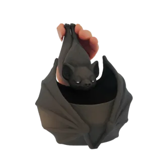 3D model of a dark gray bat hanging upside down, with its wings spread to form a planter, held by a hand.