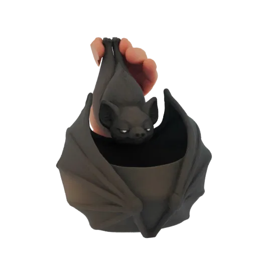 3D model of a dark gray bat hanging upside down, with its wings spread to form a planter, held by a hand.